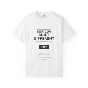 May include: A white short-sleeve t-shirt featuring black text that reads BORICUA BUILT DIFFERENT, a black box with the number 787, and the text RAISED ON THE ISLAND. BUILT FOR ANYWHERE. EST. PUERTO RICO. The design includes thin red horizontal lines.