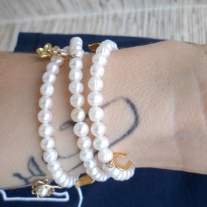 May include: A triple strand pearl bracelet with gold charms, including a flower, a horseshoe, and a wing.