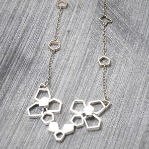 May include: A silver necklace with a geometric design. The necklace features a series of interconnected, open-frame shapes that resemble small, abstract flowers.