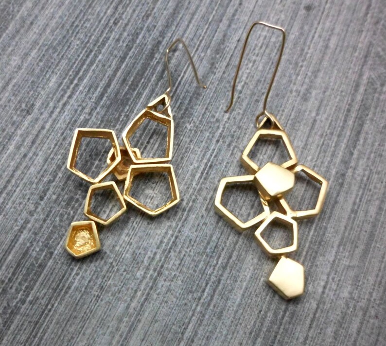 May include: A pair of gold geometric earrings with a honeycomb design. Each earring features multiple interconnected hexagonal shapes.