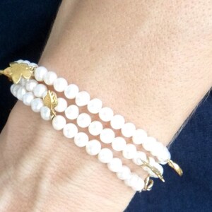 May include: A triple strand pearl bracelet with gold leaf accents. The bracelet is made of white pearls and has a delicate, feminine look.