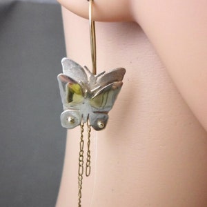 May include: Silver and gold butterfly dangle earrings with a hoop and chain detail.