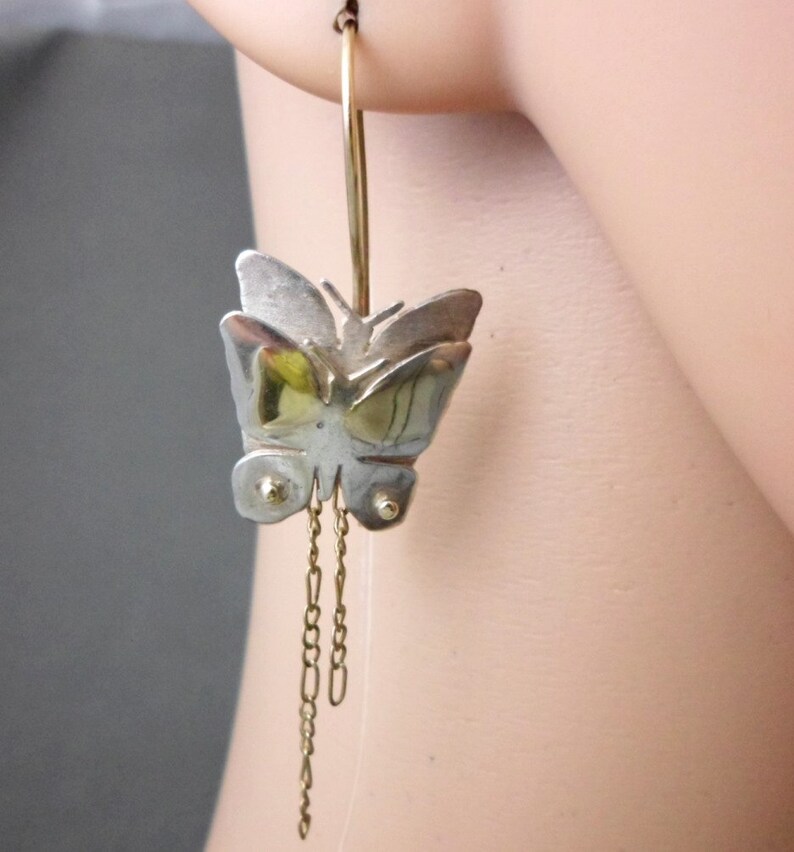 May include: Silver and gold butterfly dangle earrings with a hoop and chain detail.