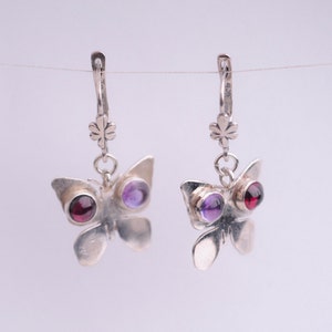 May include: Silver butterfly earrings with purple and red gemstones. The earrings have a delicate design and are perfect for adding a touch of elegance to any outfit.