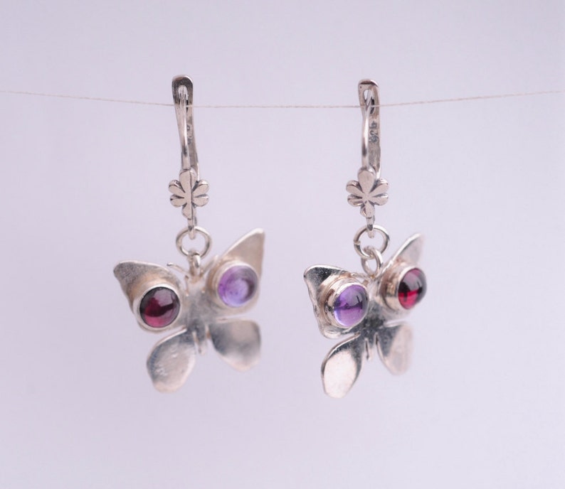 May include: Silver butterfly earrings with purple and red gemstones. The earrings have a delicate design and are perfect for adding a touch of elegance to any outfit.