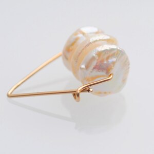 May include: A gold wire ring with a large, iridescent white pearl attached. The pearl is made up of several layers, creating a unique and textured look.