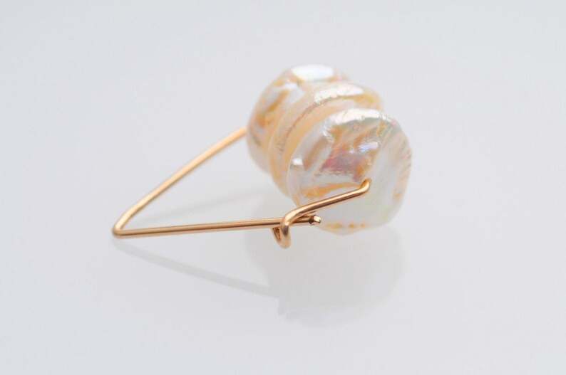 May include: A gold wire ring with a large, iridescent white pearl attached. The pearl is made up of several layers, creating a unique and textured look.