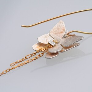 May include: A silver and gold butterfly earring with a dangling chain. The butterfly has a clear stone in the center.