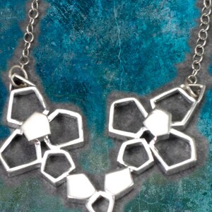 May include: A silver necklace with a geometric design. The necklace is made up of multiple interconnected hexagonal shapes.