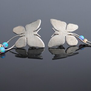 May include: A pair of silver butterfly earrings with opal accents hanging from a silver chain.