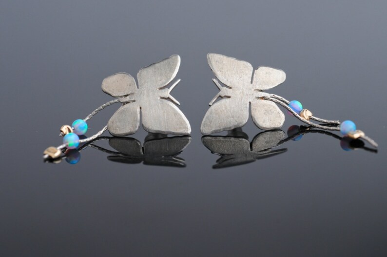 May include: A pair of silver butterfly earrings with opal accents hanging from a silver chain.