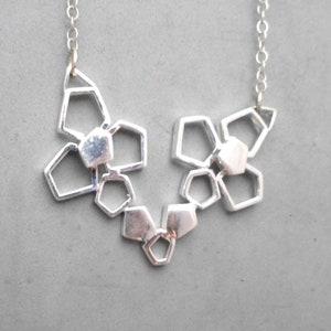 May include: A silver necklace with a geometric design featuring multiple interconnected shapes. The necklace is made of a chain and has a pendant with a geometric pattern.