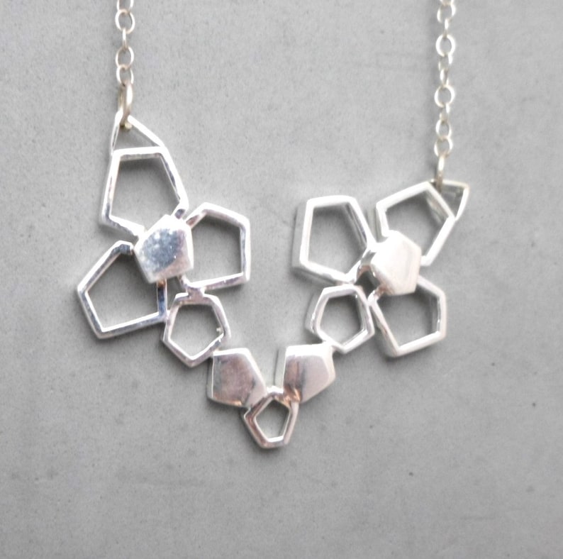 May include: A silver necklace with a geometric design featuring multiple interconnected shapes. The necklace is made of a chain and has a pendant with a geometric pattern.