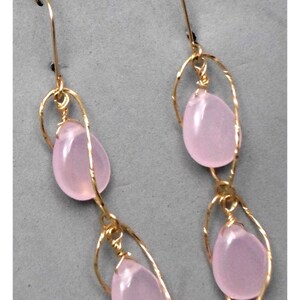 May include: A pair of gold earrings with pink gemstone drops. The earrings are made with delicate wire wrapped around the stones.