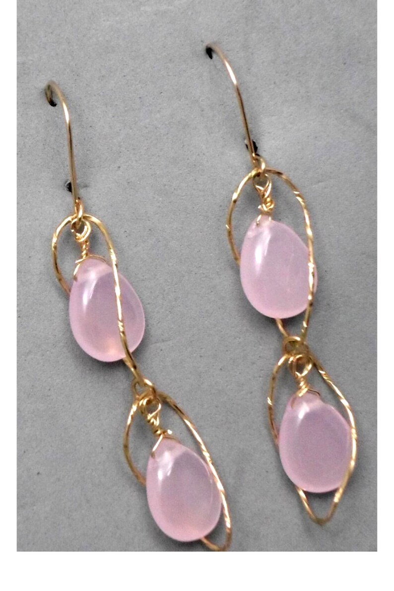 May include: A pair of gold earrings with pink gemstone drops. The earrings are made with delicate wire wrapped around the stones.