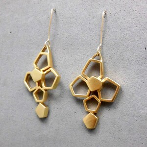 May include: A pair of gold geometric earrings with a cluster of hexagonal shapes hanging from a thin wire.