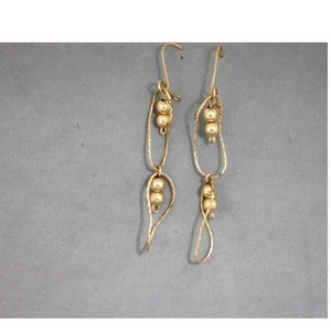 Könnte beinhalten: Ein Paar goldene Ohrringe mit drei kleinen goldenen Perlen an jedem Ohrring. Die Ohrringe sind aus dünnem, gedrehtem Draht gefertigt.