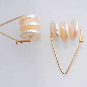 May include: A pair of gold hoop earrings with a triangular shape. Each earring features a stack of four white pearl-like beads.