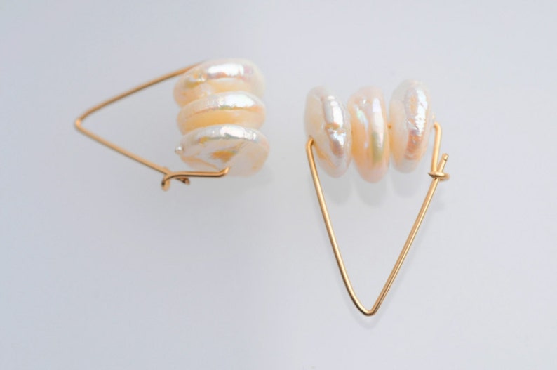 May include: A pair of gold hoop earrings with a triangular shape. Each earring features a stack of four white pearl-like beads.