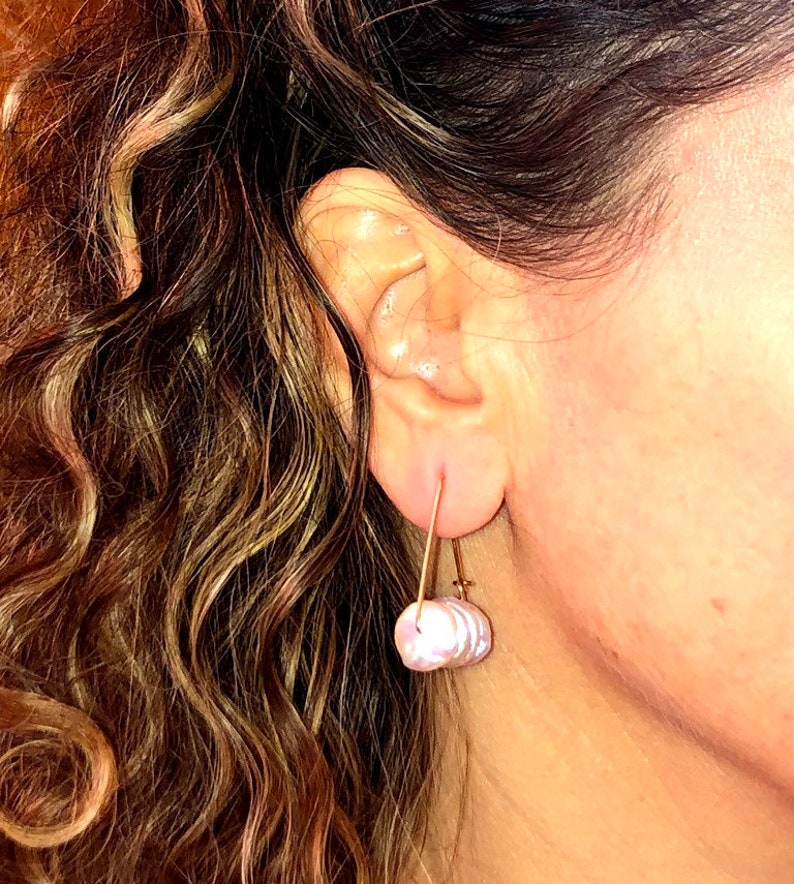 May include: A pair of earrings with a single, large, iridescent pearl-like drop on each earring. The earrings are made of gold-toned metal and have a simple, minimalist design.