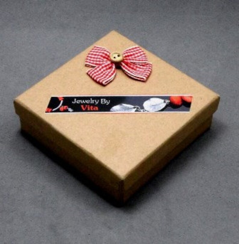 May include: A small, square, brown cardboard box with a red and white gingham bow and a button on top. The box has a label that says "Jewelry By Vita".