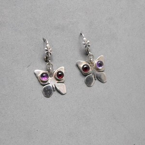 May include: A pair of silver butterfly earrings with purple and red gemstone accents.