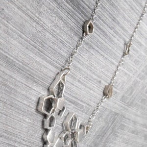 May include: A silver necklace with a geometric pendant made of interconnected hexagonal shapes. The pendant is attached to a silver chain with small hexagonal links.