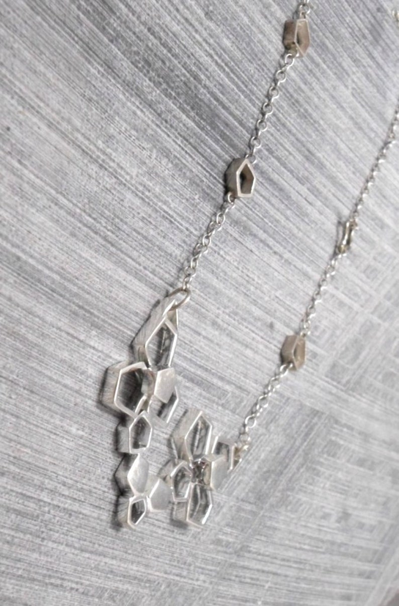 May include: A silver necklace with a geometric pendant made of interconnected hexagonal shapes. The pendant is attached to a silver chain with small hexagonal links.