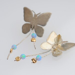 May include: Silver butterfly earrings with a dangling chain of opal beads and gold accents. The earrings are marked "925" on the back.