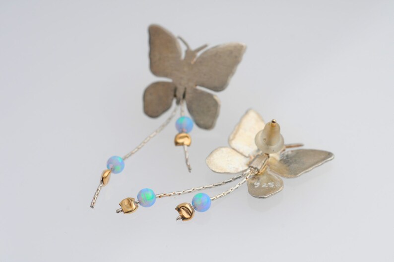 May include: Silver butterfly earrings with a dangling chain of opal beads and gold accents. The earrings are marked "925" on the back.