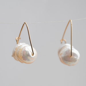 May include: A pair of gold hoop earrings with a cluster of white baroque pearls hanging from each hoop.