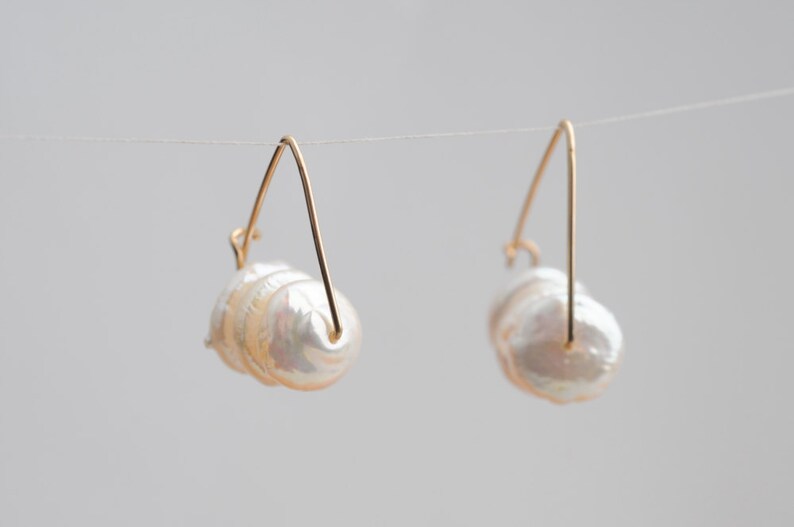 May include: A pair of gold hoop earrings with a cluster of white baroque pearls hanging from each hoop.
