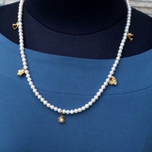May include: A white pearl necklace with gold charms in the shape of a heart, a flower, a leaf, and a butterfly.
