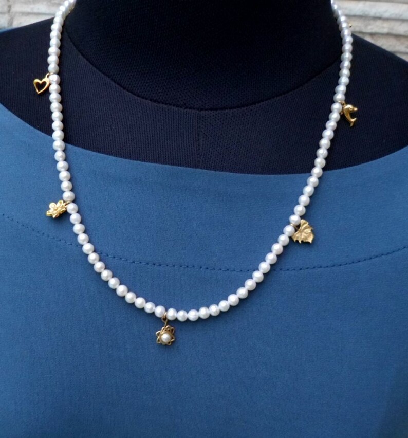 May include: A white pearl necklace with gold charms in the shape of a heart, a flower, a leaf, and a butterfly.