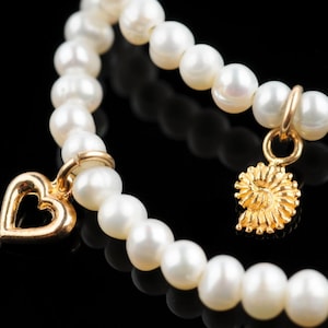 May include: A white pearl bracelet with two gold charms, one shaped like a heart and the other like a spiral.