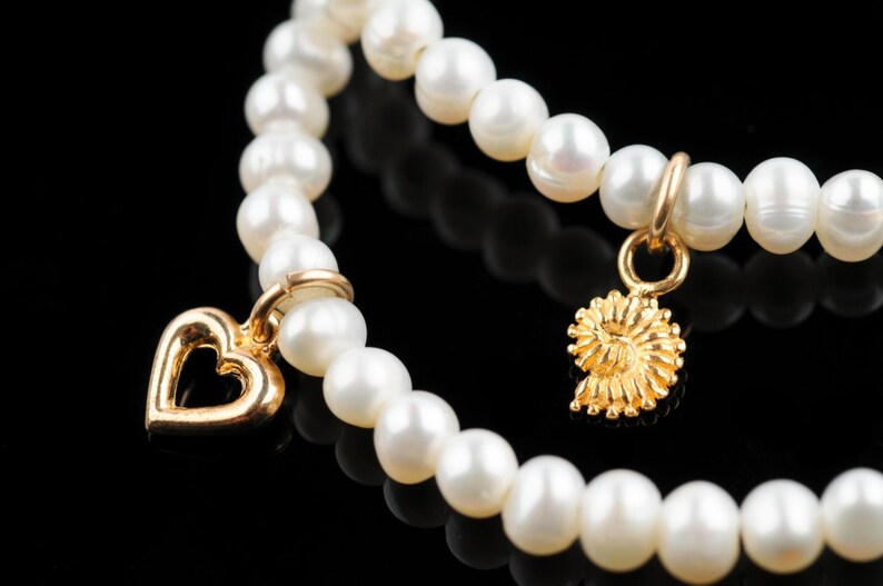 May include: A white pearl bracelet with two gold charms, one shaped like a heart and the other like a spiral.