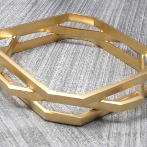 May include: Gold-toned metal bangle bracelet with a geometric design. The bracelet features an open, interlocking design with multiple hexagonal shapes. The bracelet is approximately 2.5 inches in diameter.