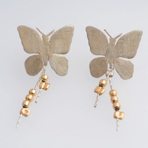 May include: A pair of silver butterfly earrings with gold bead and square charms dangling from the bottom.