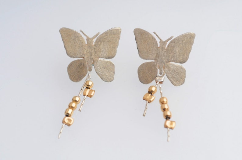 May include: A pair of silver butterfly earrings with gold bead and square charms dangling from the bottom.