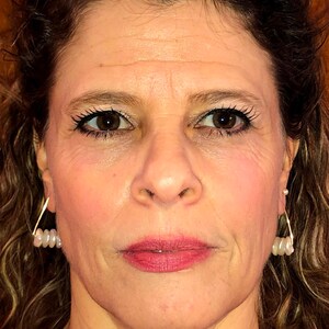 May include: A close-up of a woman's face. She has brown hair, brown eyes, and is wearing makeup. She is wearing earrings with small white pearls.