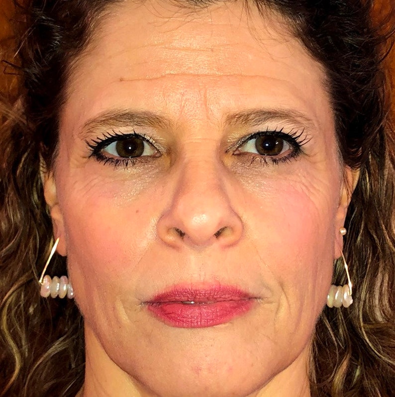 May include: A close-up of a woman's face. She has brown hair, brown eyes, and is wearing makeup. She is wearing earrings with small white pearls.