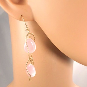 May include: Gold earrings with two pink teardrop-shaped stones hanging from a delicate wire design.