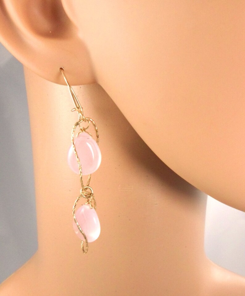 May include: Gold earrings with two pink teardrop-shaped stones hanging from a delicate wire design.