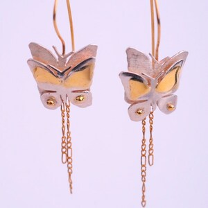 May include: A pair of gold and silver butterfly earrings with dangling chains. The butterflies are layered and have a textured finish.