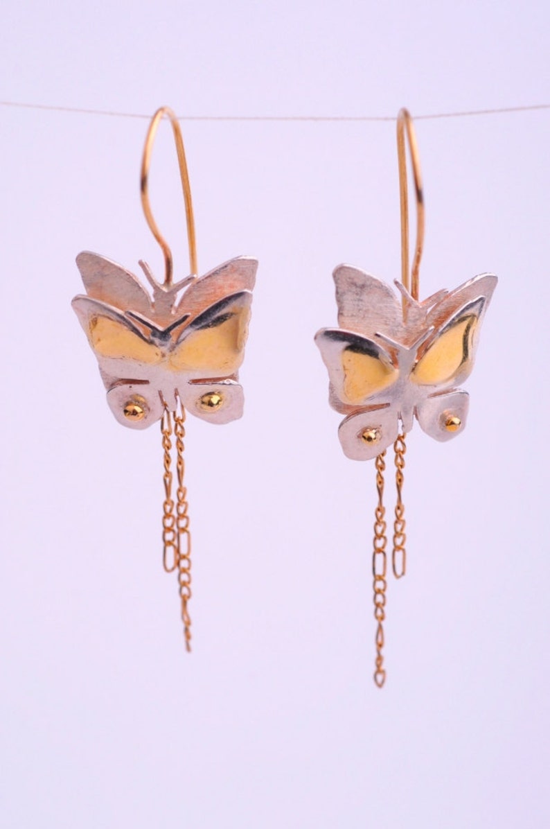 May include: A pair of gold and silver butterfly earrings with dangling chains. The butterflies are layered and have a textured finish.