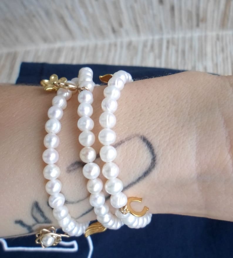 May include: A triple strand pearl bracelet with gold charms, including a flower, a horseshoe, and a wing.