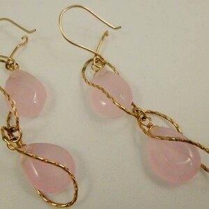 May include: A pair of gold earrings with pink teardrop-shaped stones. The earrings are made with twisted wire and have a dangling design.