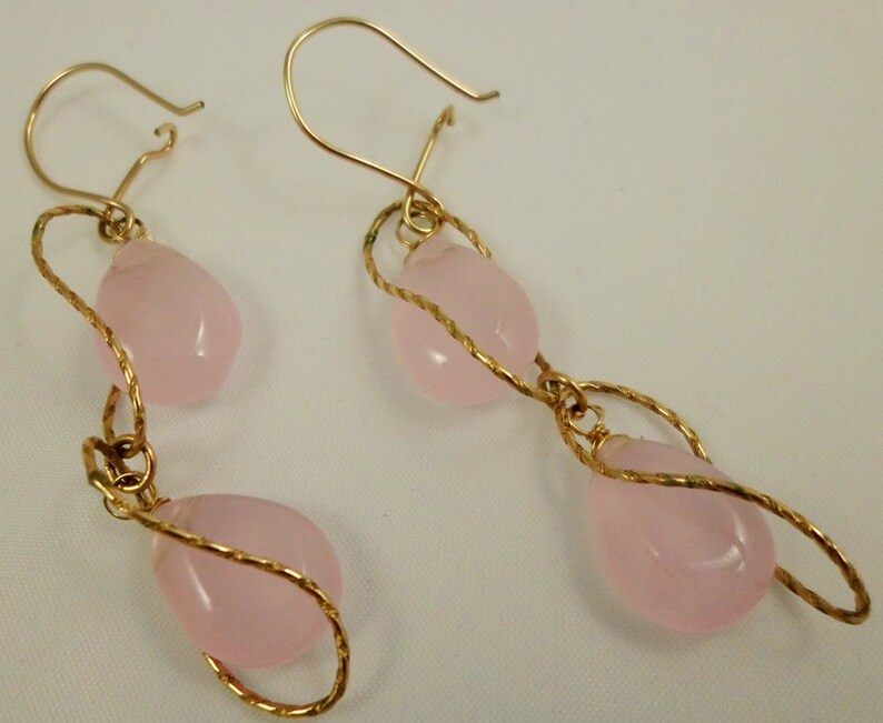 May include: A pair of gold earrings with pink teardrop-shaped stones. The earrings are made with twisted wire and have a dangling design.