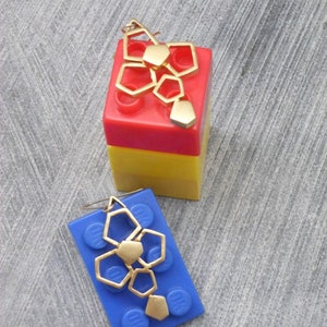 May include: Two gold geometric earrings on blue and red Lego blocks. The earrings are made of multiple connected hexagonal shapes.