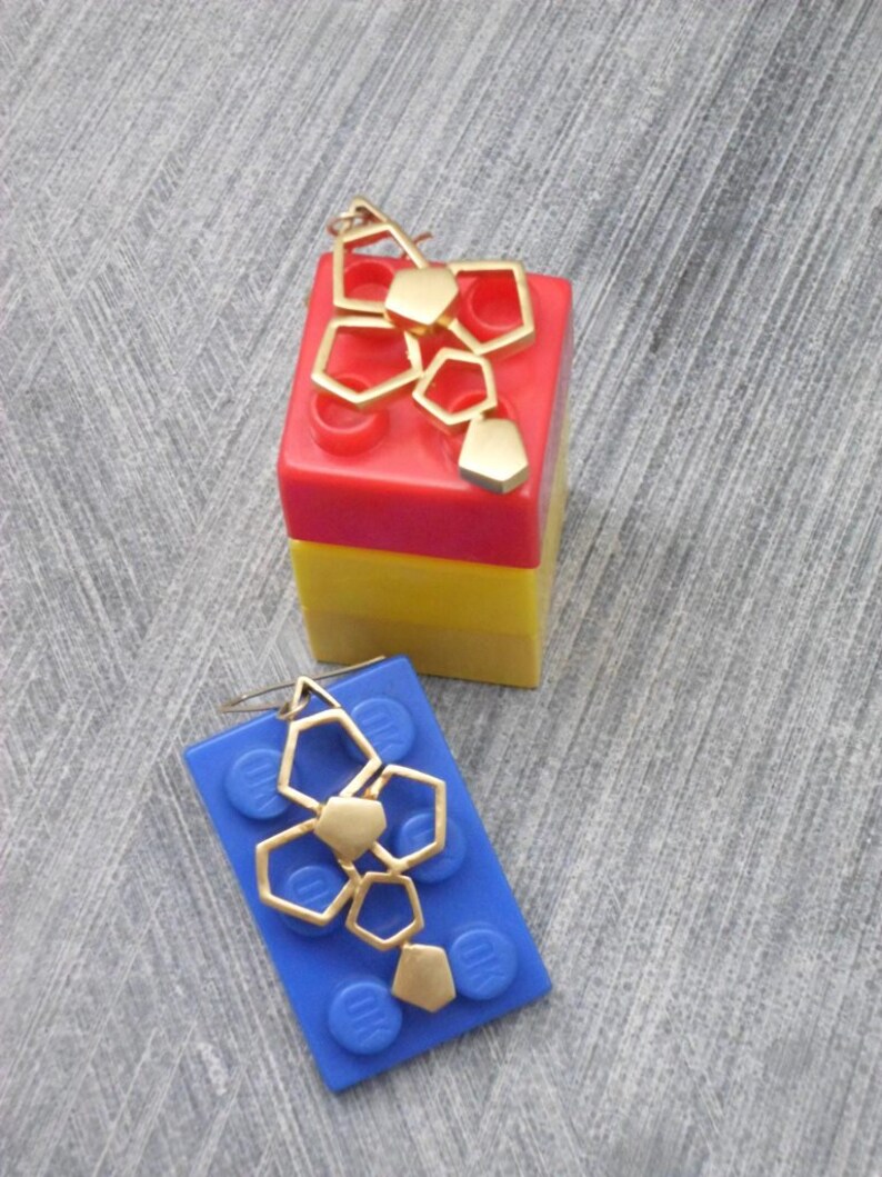 May include: Two gold geometric earrings on blue and red Lego blocks. The earrings are made of multiple connected hexagonal shapes.